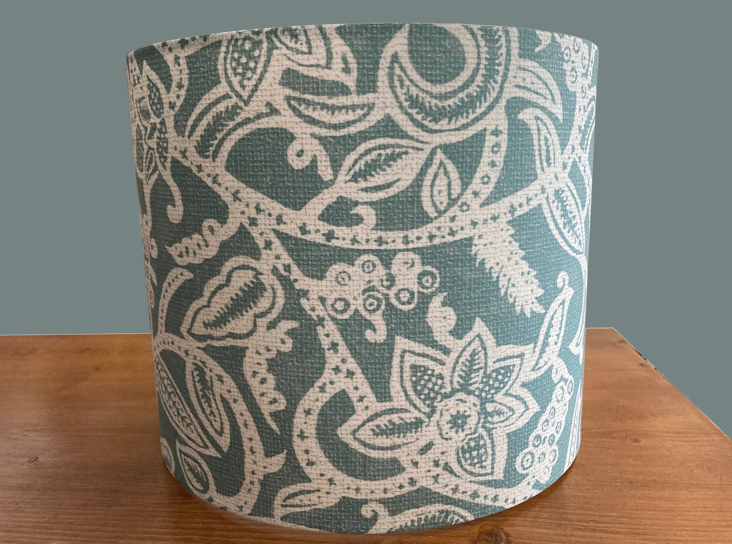 Teal and cream floral patterned drum lampshade on wooden surface